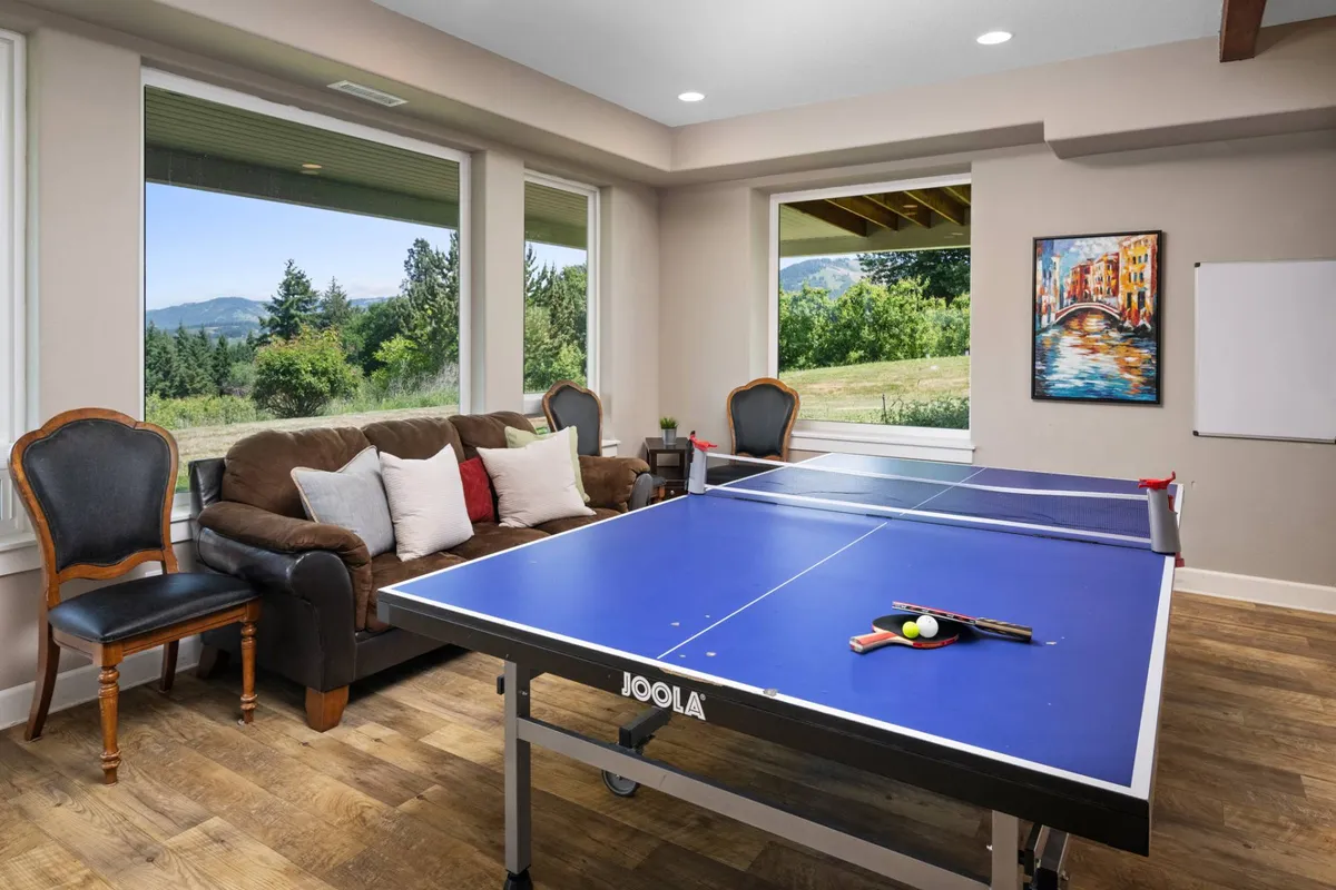 This vibrant interior image features a ping pong table as the central focus, with a comfortable couch and large windows that offer beautiful views. Colorful artwork adds a playful touch to the room, reinforcing the sense of energetic recreation and relaxation. The spacious setting invites guests to gather for games or to sit back and enjoy the scenery.