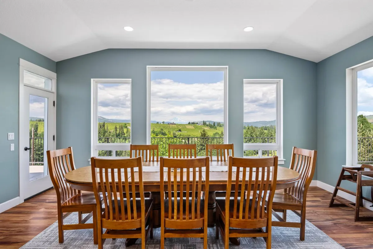 The image features a large wooden dining table surrounded by comfortable chairs, positioned by expansive windows that reveal picturesque orchard and mountain views. The warm lighting and inviting setup make it ideal for hosting family meals or gatherings, while the natural scenery serves as a stunning backdrop.