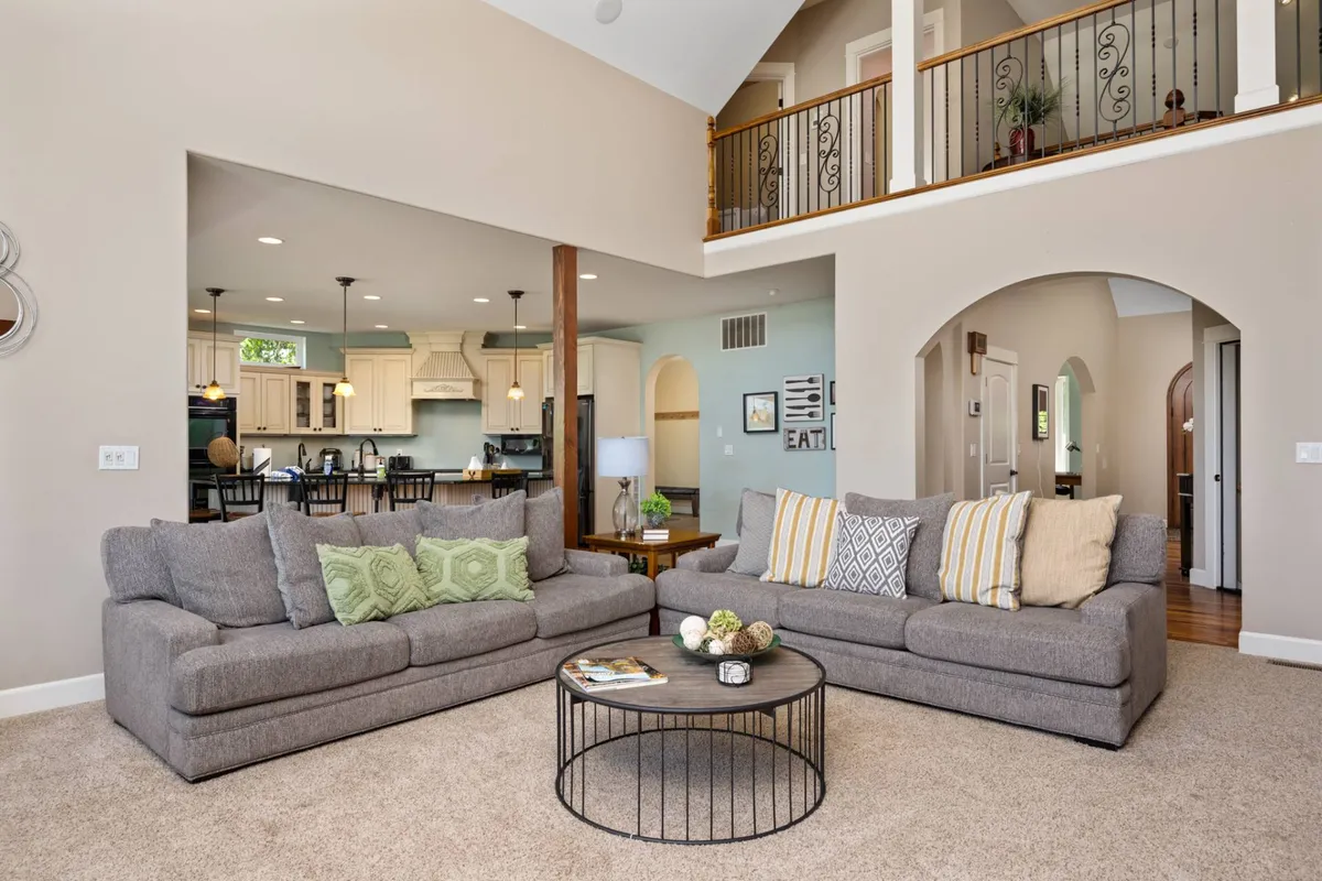 An open-concept living space with sofas and a coffee table, blending seamlessly into an adjacent kitchen area. The presence of a balcony railing implies direct access to the outdoors, creating a transition zone between sophisticated interiors and scenic exterior views.