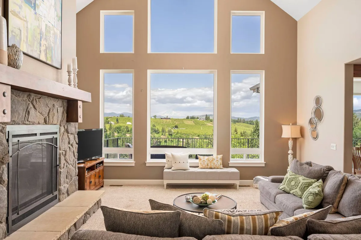 This interior shot highlights a cozy seating area with plush furnishings arranged around a stone fireplace, set against large windows that showcase vineyard views. The tranquil, welcoming atmosphere is enhanced by both the elegant décor and the warmth of the fireplace, inviting relaxation and conversation.