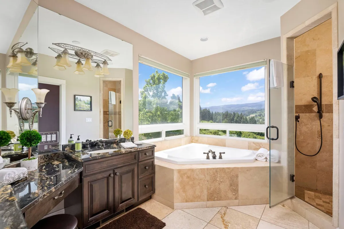 A spa-like bathroom with a large soaking bathtub positioned by expansive windows offering stunning sunrise views over the landscape. The vanity and mirror add to the modern, tranquil atmosphere.