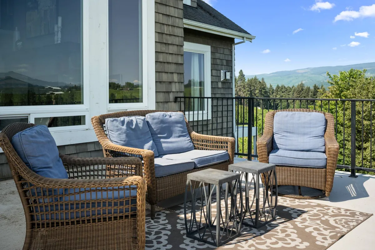 This exterior image displays a cozy outdoor seating area with wicker chairs and a metal coffee table, overlooking picturesque landscape views. The setting is ideal for winding down with friends at sunset or stargazing under the open sky, capturing the tranquility and beauty of the outdoors.