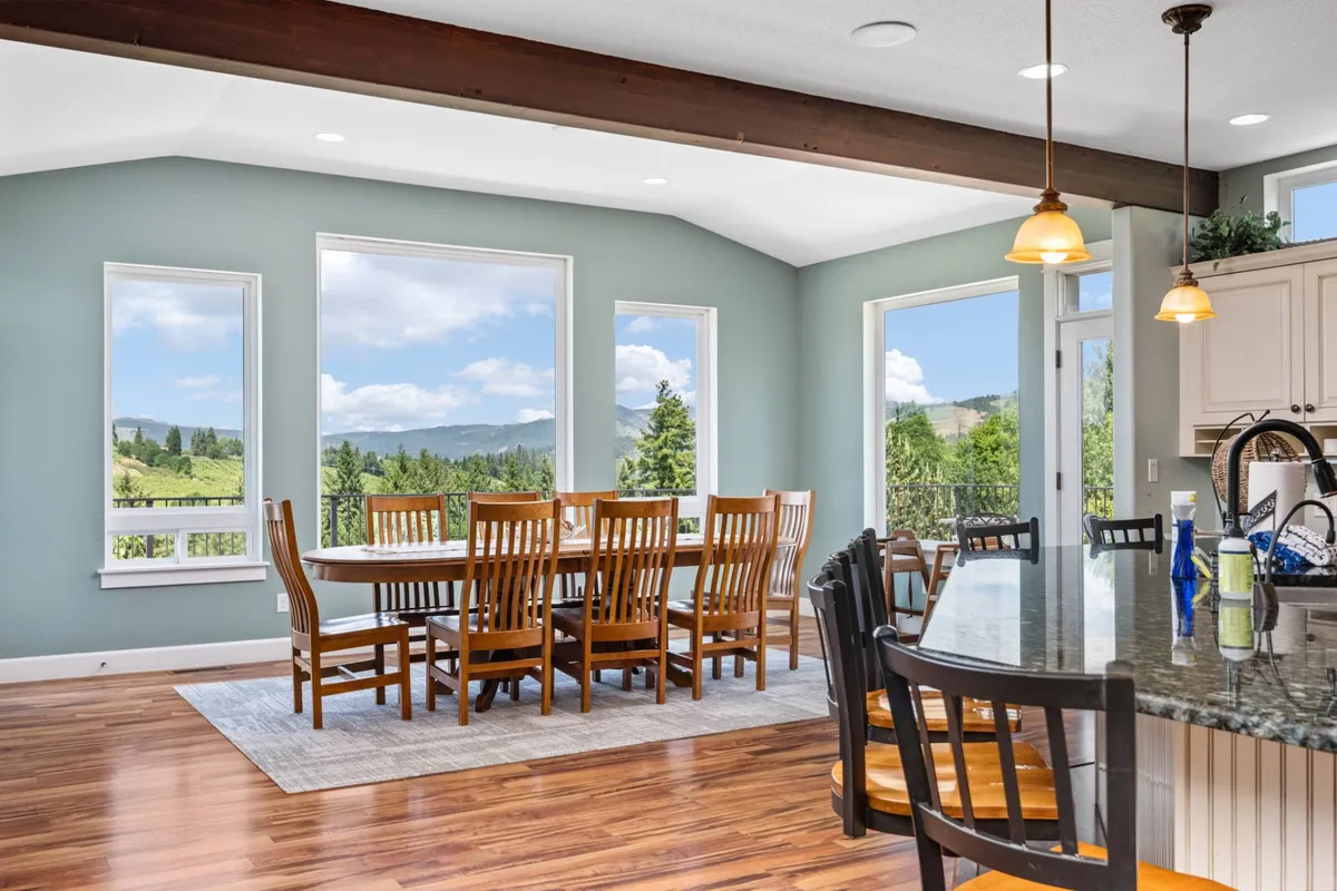 A wide-angle view of the main living space that seamlessly blends a large dining table, kitchen island, and floor-to-ceiling windows. The room is flooded with natural light, and the outdoor scenery forms a dramatic backdrop, while the elegant table settings and comfortable furnishings invite festive gatherings.