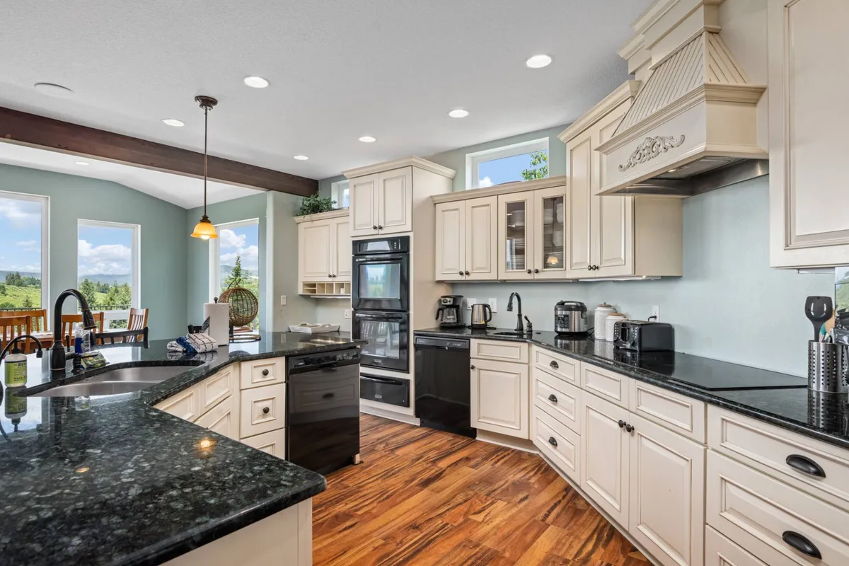 A warm and inviting kitchen scene with a prominent kitchen island, sleek black appliances, ample cabinetry, and windows that offer scenic views. The space is set for baking, hosting dinner parties, or sipping coffee while enjoying the view, capturing everyday and special moments alike.