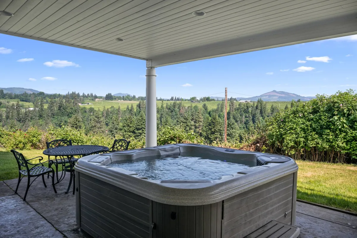 Set outdoors, this image features a private hot tub surrounded by outdoor seating, all overlooking a scenic landscape of rolling hills. The tranquil setting encourages relaxation, with space for stargazing or morning coffee, and hints at the expansive deck just beyond.
