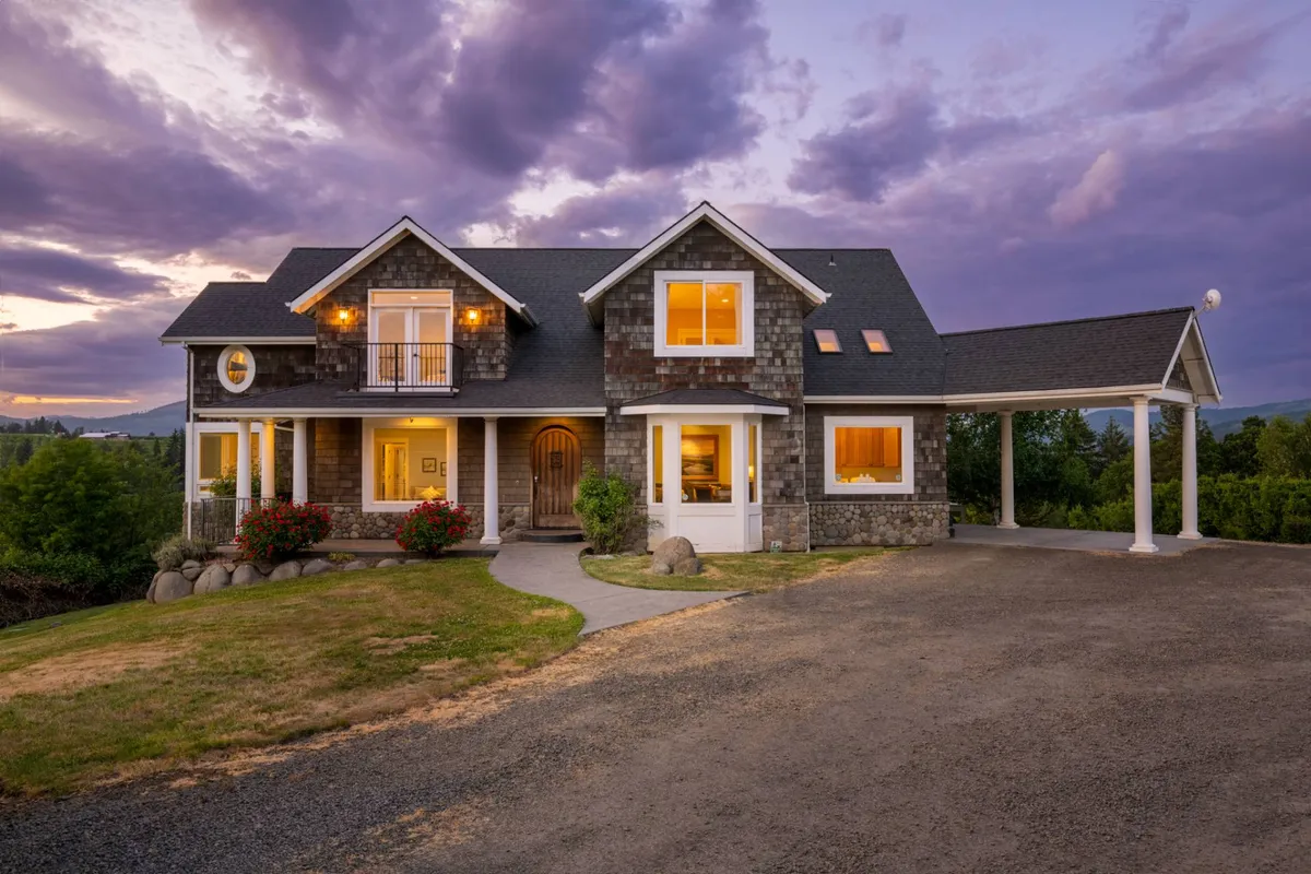 This image features the exterior front porch of the estate, with large windows and vibrant flower beds. The scene is bathed in warm sunset light, creating an inviting atmosphere perfect for evening relaxation or family gatherings. The porch looks out onto the surrounding grounds, hinting at the open space available for walks and exploration.