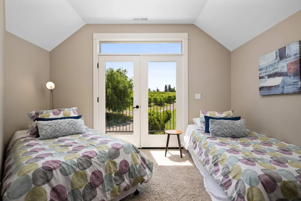 A tranquil bedroom with two beds facing double French doors that lead directly outside. Soft morning light pours in, inviting guests to step out and begin a day of adventure in the fresh country air.