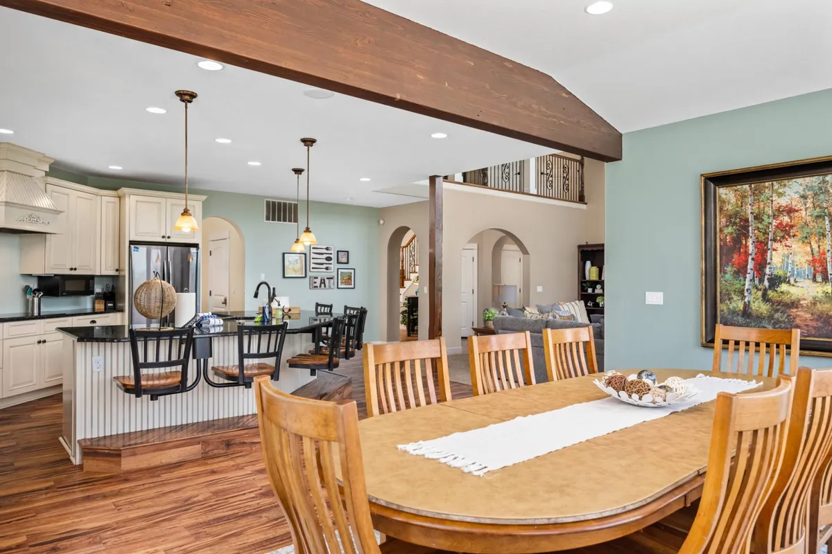 A bright and homey open-plan space that connects a dining table, kitchen island, colorful artwork, and inviting light fixtures. The layout encourages family meals, guest entertaining, and relaxed cooking, reflecting a seamless flow between spaces for both casual and formal gatherings.